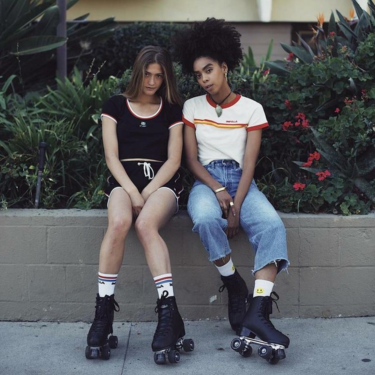 picture of two girls sitting on a concrete in front flowers wearing black impala skates 