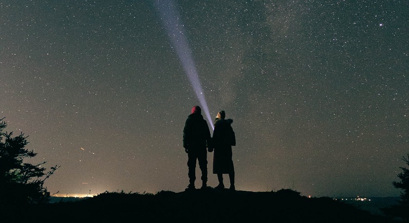 picture of two people standing on a cliff with led flashlight pointing to the stars