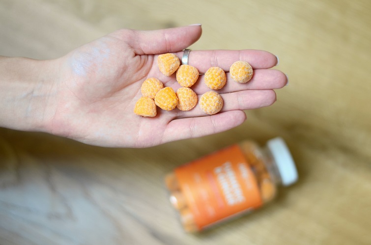 picture of an orange jellybean pills in a hand of a person up from the orange bottle on the table   