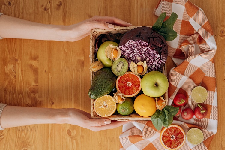 picture of person holding a box with vegetables and fruits on a wooden table 