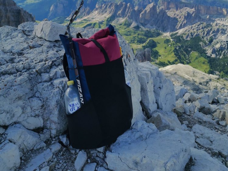 Frameless red-black backpack on a rock with a bottle of a water in the side pocket