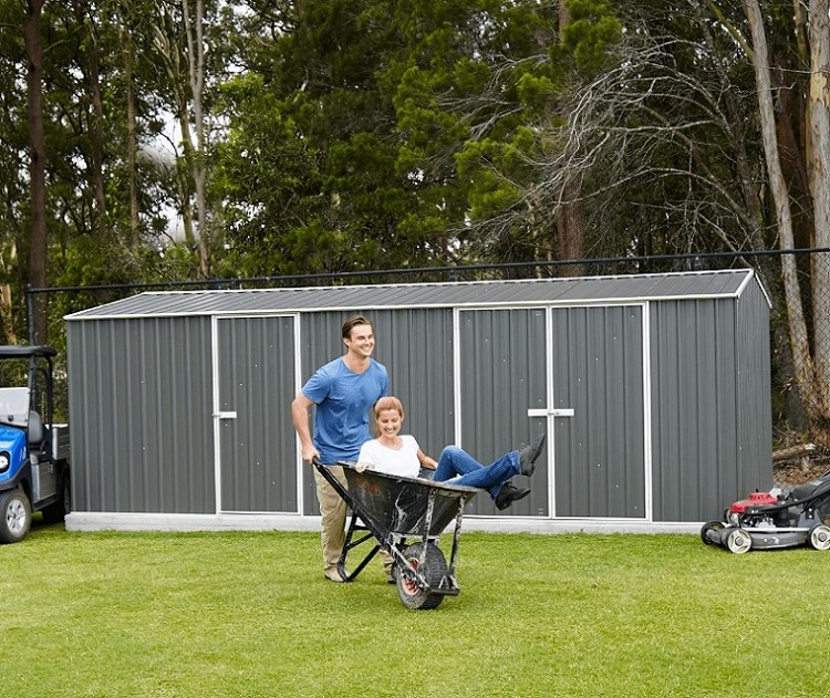 man pushing woman in wheelbarrow in front of garden shed 