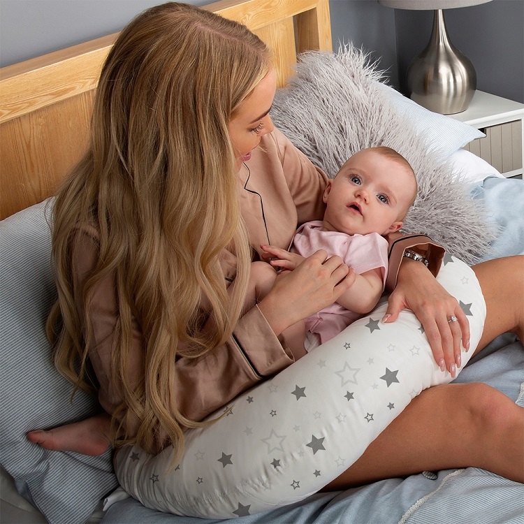 picture of a woman in bed holding a baby in a feeding pillow 