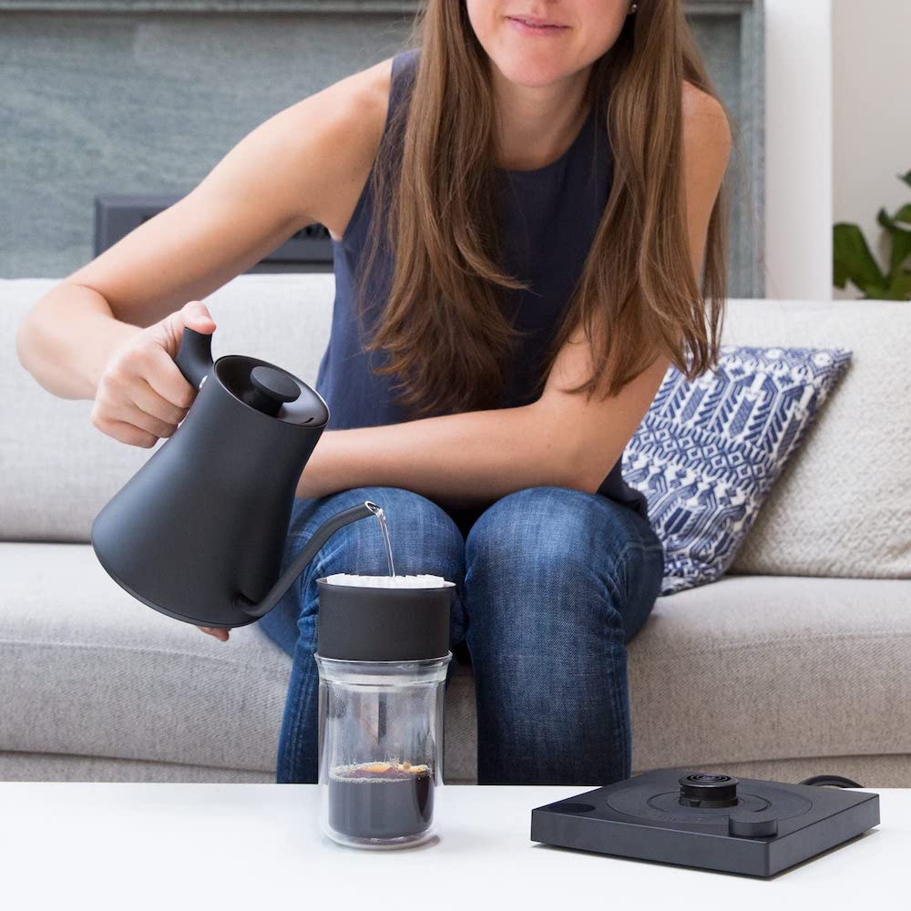 electric coffee kettle and woman whos holding it and pouring into transport coffee cup