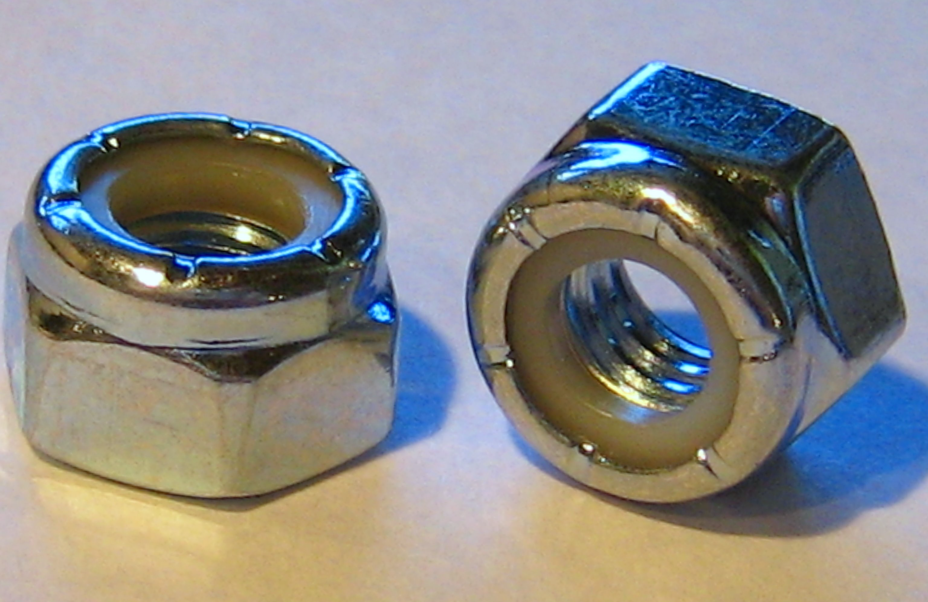 Two metal nyloc nuts, one with a blue nylon insert, side by side on a white surface.